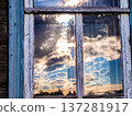 Setting sun and curly clouds reflected in an old rustic window 137281917