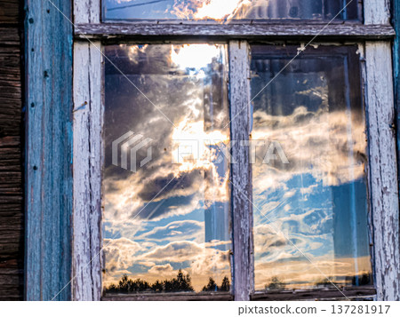 Setting sun and curly clouds reflected in an old rustic window 137281917