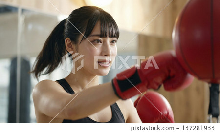 一位微笑的日本女子在健身房做拳擊練習，擊打著拳擊球。 137281933
