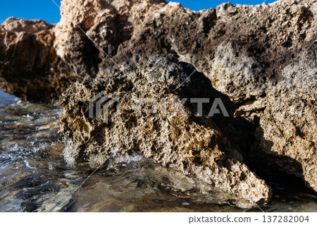 A large rock formation on the shore of a red sea. A weathered limestone cliff on a crystal-clear seashore with calm blue water. Egypt. 137282004