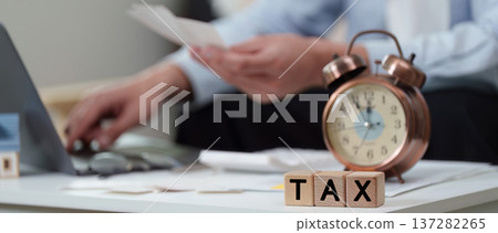 Tax Preparation. Individual managing tax documents with clock and laptop. Tax Preparation. Individual managing tax documents with clock and laptop. 137282265