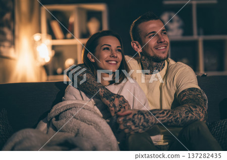 tattooed couple enjoying cozy movie night at home, sitting on couch with soft blankets, warm tattooed couple enjoying cozy movie night at home, sitting on couch with soft blankets, warm 137282435