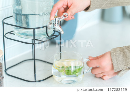 一位女士正在廚房檯面上從飲水機倒排毒水。 一位女士正在廚房檯面上從飲水機倒排毒水。 137282559