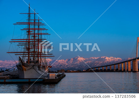 The pink Abenrot peaks of the Tateyama mountain range with Shinminato Bridge and Kaiwomaru in the foreground from Kaiwomaru Park in the evening 137283506