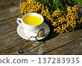 A hot tansy infusion, known for its antispasmodic and choleretic effects, is served in an elegant white cup against a natural wooden background. 137283935