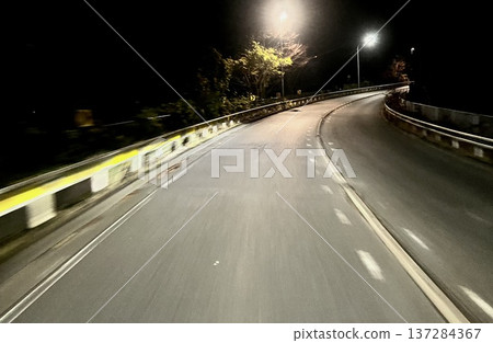 A road running through a curved mountain road at night. Night road scenery illuminated by street lights. A road running through a curved mountain road at night. Night road scenery illuminated by street lights. 137284367