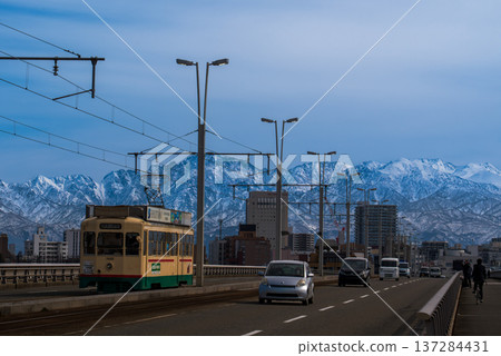 A tram crossing the Kureha Bridge in Toyama City with the snow-capped Tateyama mountain range in the background A tram crossing the Kureha Bridge in Toyama City with the snow-capped Tateyama mountain range in the background 137284431