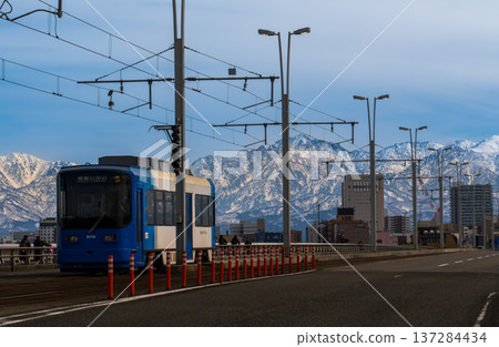 A tram crossing the Kureha Bridge in Toyama City with the snow-capped Tateyama mountain range in the background 137284434