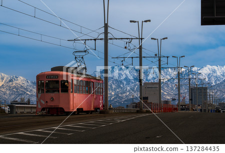 一輛電車駛過富山市的久禮羽橋,背景是白雪皚皚的立山山脈。 一輛電車駛過富山市的久禮羽橋,背景是白雪皚皚的立山山脈。 137284435