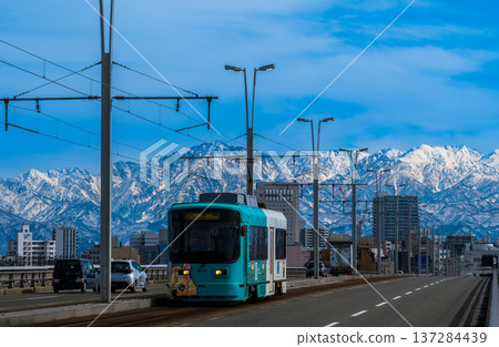 A tram crossing the Kureha Bridge in Toyama City with the snow-capped Tateyama mountain range in the background A tram crossing the Kureha Bridge in Toyama City with the snow-capped Tateyama mountain range in the background 137284439
