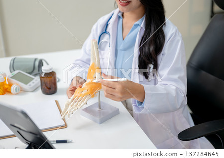 Close up woman doctor teaching or explaining bone model on video call in tablet on diagnosis table. Close up woman doctor teaching or explaining bone model on video call in tablet on diagnosis table. 137284645