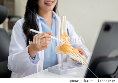 Close up of woman doctor teaching explaining bone model to video call in tablet on diagnosis table. Close up of woman doctor teaching explaining bone model to video call in tablet on diagnosis table. 137284646