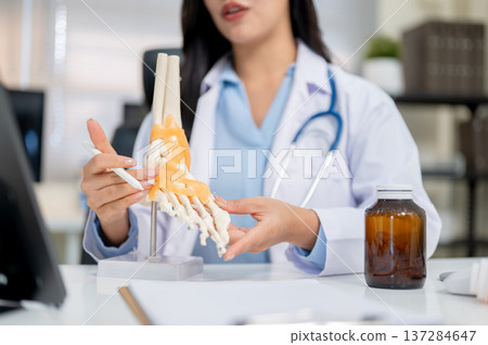 Close up of a woman doctor explaining bone model to tablet aside medicine bottle at diagnosis table. Close up of a woman doctor explaining bone model to tablet aside medicine bottle at diagnosis table. 137284647