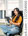 Smiling asian woman freelancer office worker writing in tablet sitting on leather chair at company. 137284666