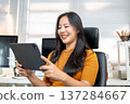 Asian woman freelancer office worker looking watching on tablet sitting on leather chair in company. 137284667