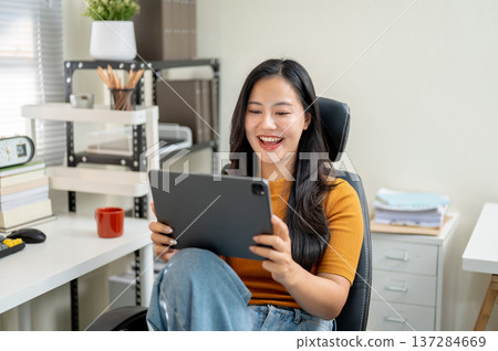 Asian woman freelancer or office worker watching video on tablet sitting on leather chair at company Asian woman freelancer or office worker watching video on tablet sitting on leather chair at company 137284669
