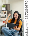 Excited asian woman cheering sport on tablet making fist sit on leather chair at home office company 137284670