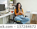 Smiling asian woman freelancer holding looking at phone sits on leather chair at home office company 137284672