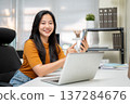 Asian woman freelancer office worker holding using smartphone aside laptop sitting at company table 137284676