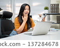 Asian woman freelancer or office worker holding phone looking at laptop as sitting at company table. 137284678