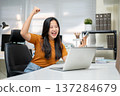 Excited asian woman office worker holding phone making a fist and looking at laptop on company table 137284679