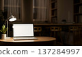 White screen laptop and lamp aside plant on round wooden table across window in dim library at night 137284997