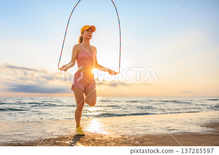 Fit woman jumping rope at the beach during summer vacation Fit woman jumping rope at the beach during summer vacation 137285597