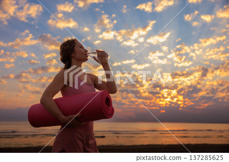 Athlete woman drinking water at the beach during summer vacation Athlete woman drinking water at the beach during summer vacation 137285625