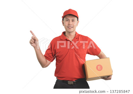 Friendly delivery person in red uniform pointing upwards while holding a package box isolated on white background for logistics or shipping services 137285847