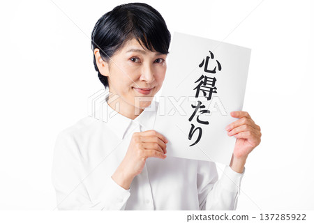 A senior woman holding a piece of paper with the word "knowledge" written on it in both hands and grinning 137285922