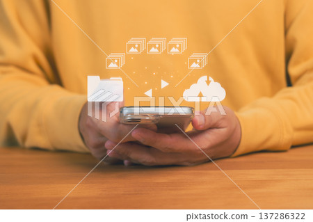 Hands holding a smartphone with icons of folders, images, and cloud upload, representing digital file transfer, cloud storage, mobile backup, data management, and seamless multimedia synchronization. Hands holding a smartphone with icons of folders, images, and cloud upload, representing digital file transfer, cloud storage, mobile backup, data management, and seamless multimedia synchronization. 137286322