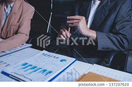 Two business people talk project strategy at office meeting room. Businessman discuss project planning with colleague at modern workplace while having conversation and advice on financial data report. 137287620