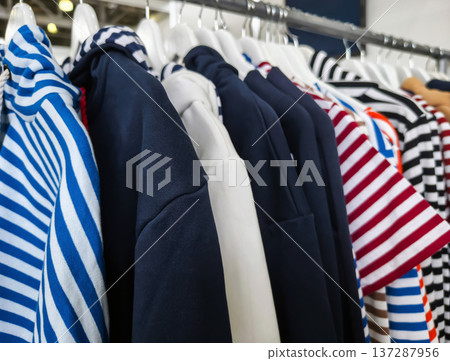 Clothes and vests hanging on a rack in a store showing various striped patterns and colors during daylight 137287956