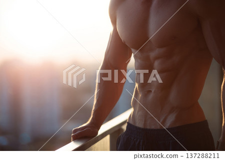 muscular man front view showing abs while standing on balcony overlooking city, soft morning muscular man front view showing abs while standing on balcony overlooking city, soft morning 137288211