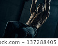 athletic man with visible abs performing hanging leg raises in gym, focused expression, dramatic 137288405