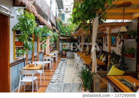 Cozy courtyard cafe with lush greenery and wooden tables Cozy courtyard cafe with lush greenery and wooden tables 137290006