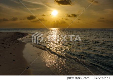 Golden sun dips low over calm ocean waves 137290334