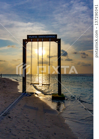 Sunset glows behind a swing at the beach edge Sunset glows behind a swing at the beach edge 137290341