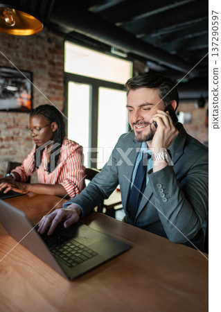 Businessman talking on smartphone while working on laptop Businessman talking on smartphone while working on laptop 137290597