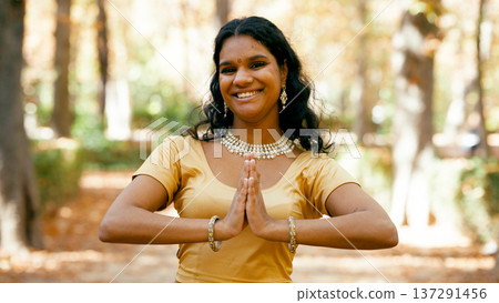 Indian woman smiling doing namaste greeting in park Indian woman smiling doing namaste greeting in park 137291456