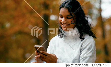 Indian woman smiling using smartphone in autumn park Indian woman smiling using smartphone in autumn park 137291489