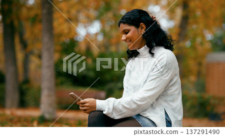 Indian woman smiling using smartphone in autumn park Indian woman smiling using smartphone in autumn park 137291490