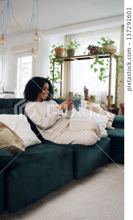 African American woman relaxing on sofa using phone African American woman relaxing on sofa using phone 137291601