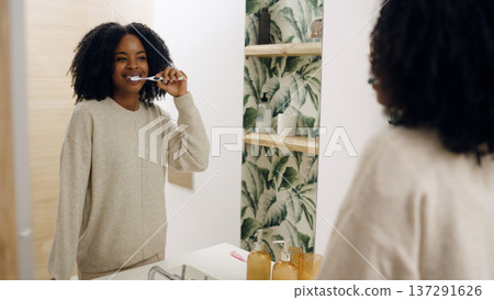 Young woman brushing teeth in modern bathroom mirror Young woman brushing teeth in modern bathroom mirror 137291626