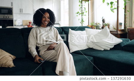 Smiling woman relaxing on couch watching tv Smiling woman relaxing on couch watching tv 137291630
