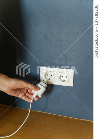 Hand plugging white charger into wall outlet Hand plugging white charger into wall outlet 137292236