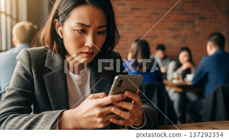 Asian businesswoman using smartphone in modern cafe with brick wall background during work break 137292354