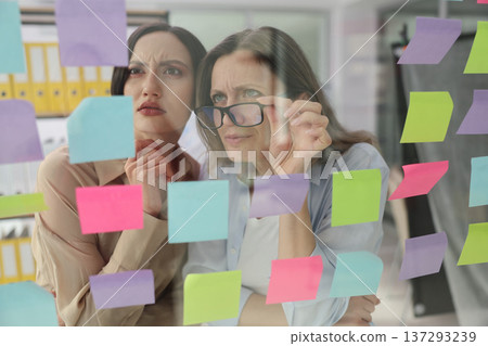 Team brainstorming ideas through colorful sticky notes in a modern office setting during the day Team brainstorming ideas through colorful sticky notes in a modern office setting during the day 137293239