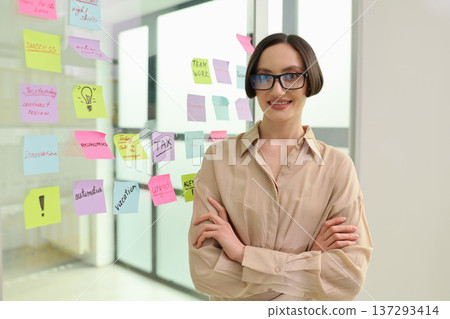 Creative professional smiles confidently in a modern office surrounded by colorful sticky notes during a collaborative session 137293414