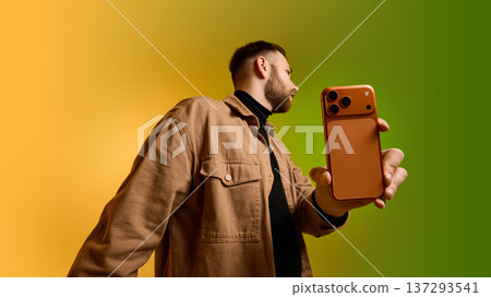 Man presenting smartphone toward camera on yellow green gradient background. 137293541